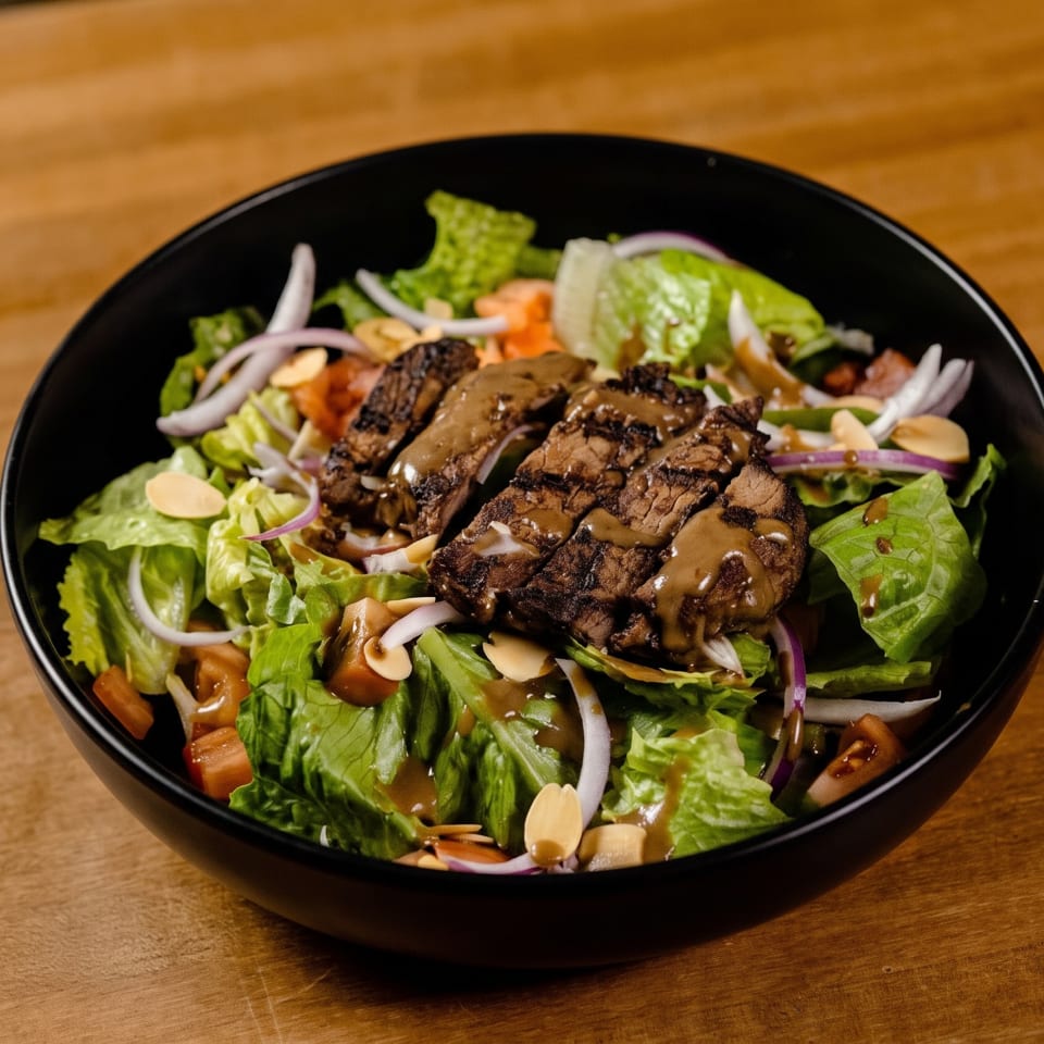 Grilled steak salad with lettuce, red onion, almonds, and dressing in a black bowl.