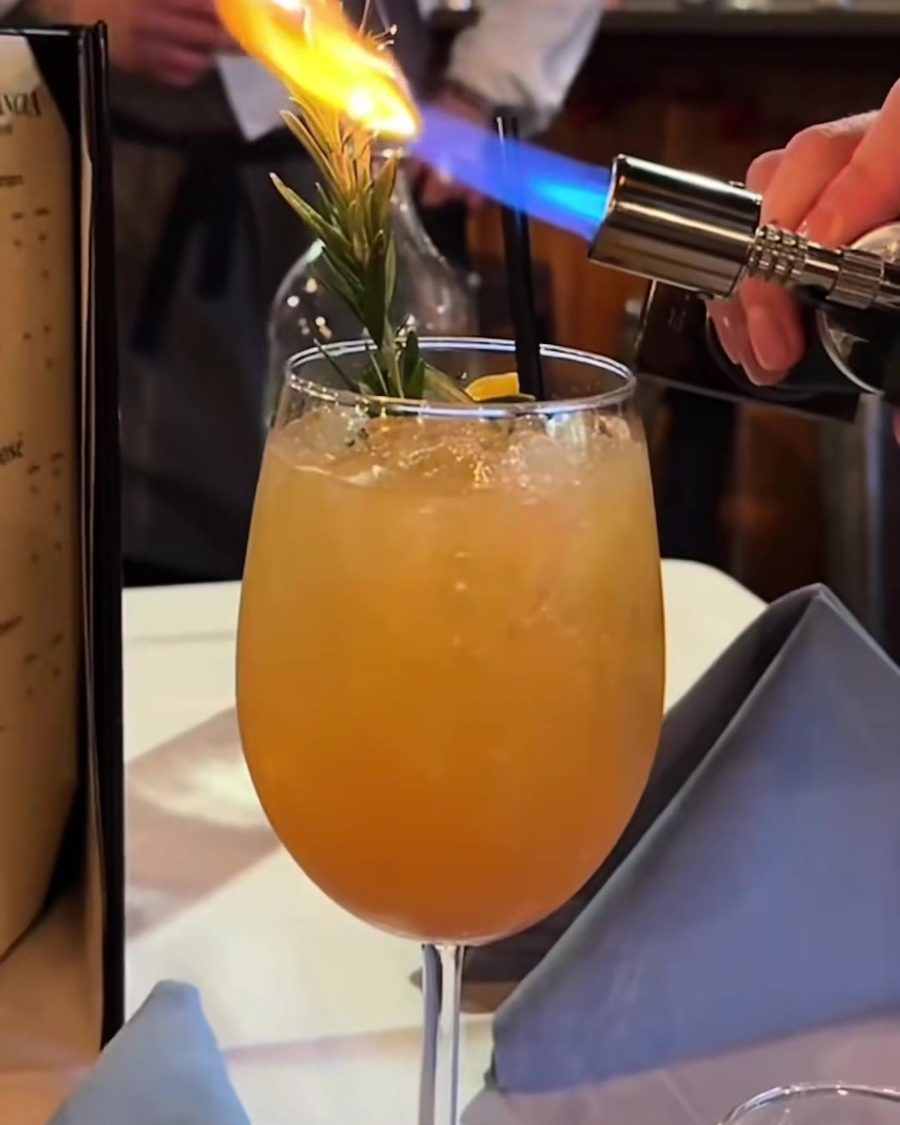 A cocktail with rosemary being finished with a torch