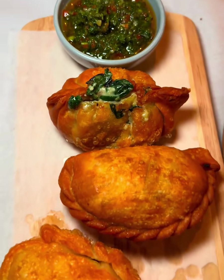 Golden empanadas with chimichurri on a wooden board