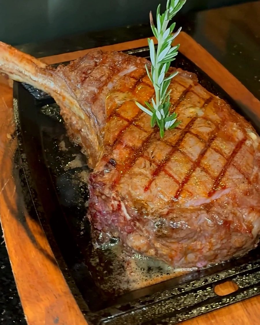 Tomahawk steak with a sprig of rosemary on a wooden board
